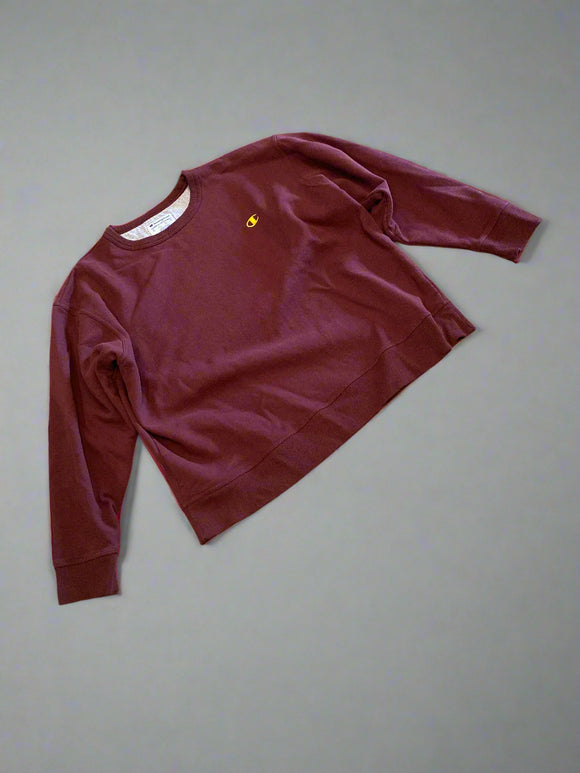 Maroon sweatshirt with a small yellow logo on a wooden floor