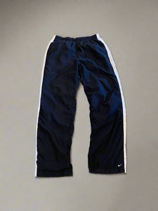 Pair of black track pants with white trim on a beige concrete floor