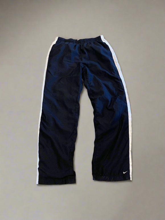 Pair of black track pants with white trim on a beige concrete floor