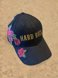 Black cap with 'Hard Rock' text and floral designs on a concrete surface