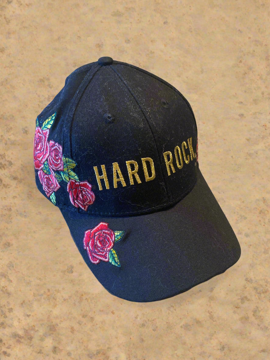 Black cap with 'Hard Rock' text and floral designs on a concrete surface