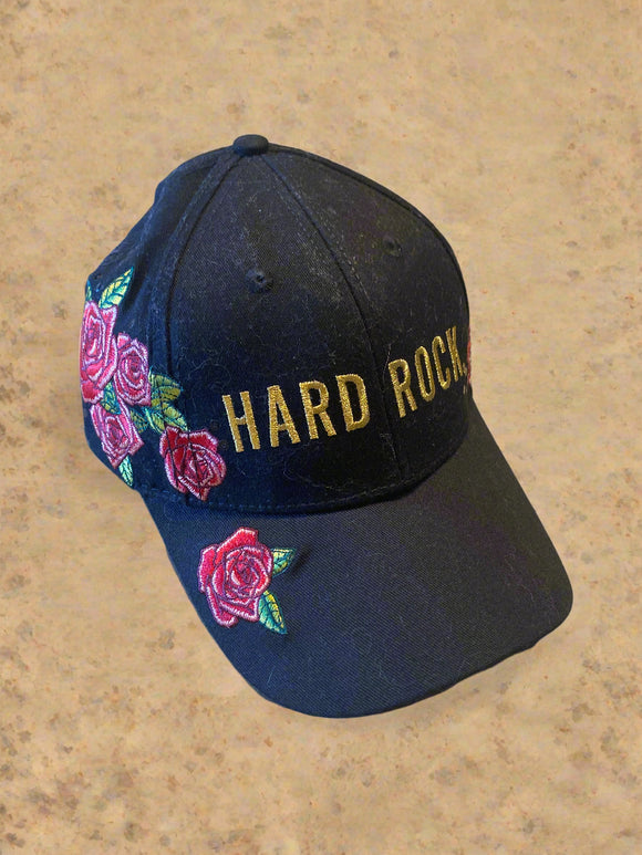 Black cap with 'Hard Rock' text and floral designs on a concrete surface