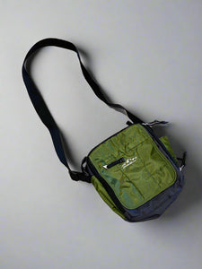 A green nylon messenger bag with a black strap and zipper, displayed on a textured surface.