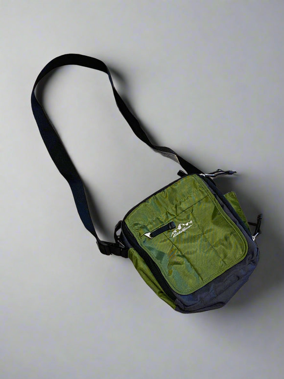 A green nylon messenger bag with a black strap and zipper, displayed on a textured surface.