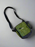 A green nylon messenger bag with a black strap and zipper, displayed on a textured surface.